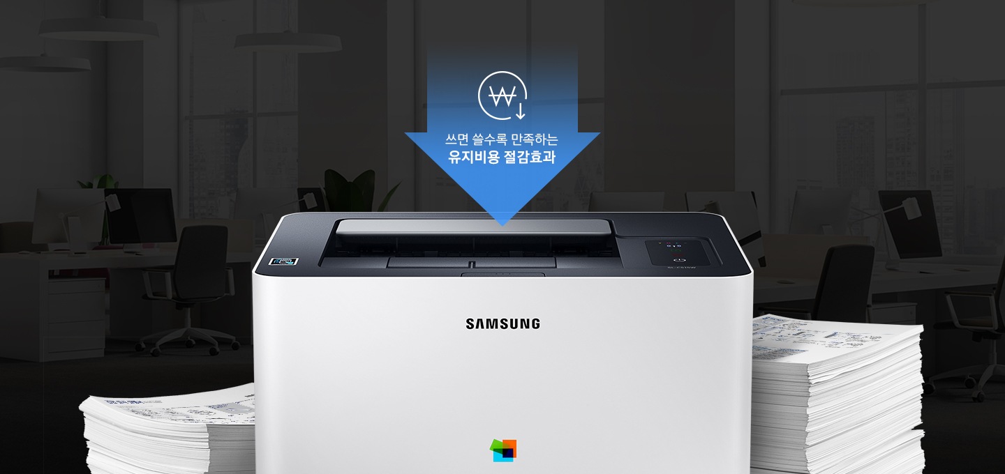 어두운 사무실 배경에 이미지 중간에는 제품 정면 이미지가 놓여있고 제품 이미지 양옆으로는 종이가 쌓여있습니다. 제품 이미지 상단에는 아래로 내려오는 파란 색상에 화살표와 화살표 안에 쓰면 쓸수록 만족하는 유지비용 절감효과 텍스트와 동그라미 안에 원 표시와 오른쪽 하단에 아래로 내려가는 아이콘이 있습니다.