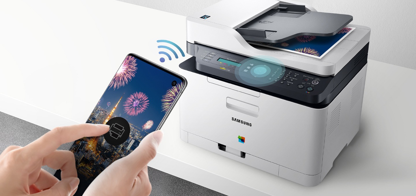 하얀색 책상 위에 제품을 오른쪽 위에서 내려본 이미지가 중간에 배치하여 있고 이미지 왼쪽 부분에 스마트폰 화면에 프린터 아이콘을 누르고 있는 사람의 손이 배치하여 있습니다.