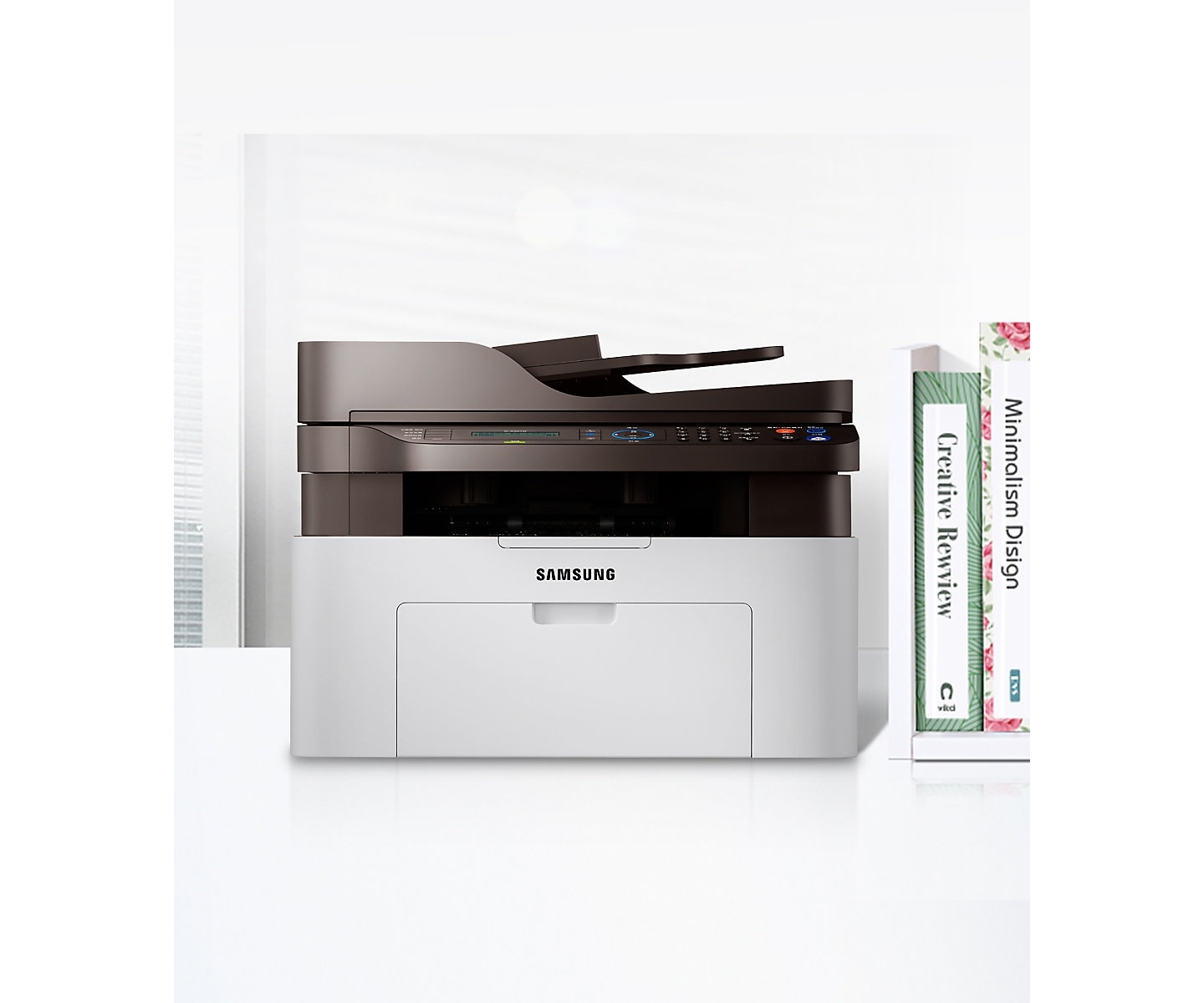 좌측에는 SL-M2077F 모델이 있고 오른쪽에는 책이 꽂혀져 있다.