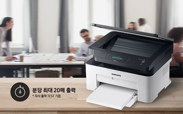 배경에는 바쁘게 회의를 하는 사람들의 모습, 바쁘게 지나가는 사람들의 모습이 흐릿하게 나와 있으며 이미지 오른쪽 부분에는 제품 오른쪽 위에서 내려본 이미지가 배치하여 있고이미지 왼쪽 하단에 분당 최대 20매 출력, 자사 출력 TEST 기준 텍스트가 쓰여 있으며, 타이머 아이콘이 나와있습니다.