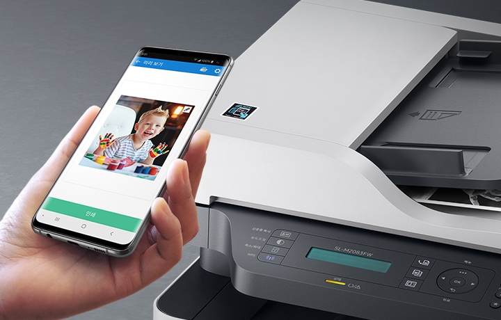 검정 색상의 나무 책상에 제품의 왼쪽 위에서 내려본 이미지가 있고 스마트폰을 제품 이미지 상단에 NFC 태그 스티커가 붙어있는 부분에 태그하는 이미지입니다.