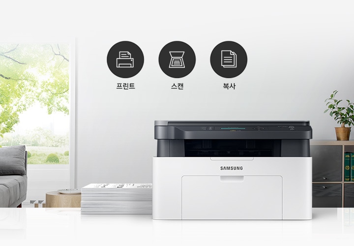 이미지 왼쪽에는 푸른 나무가 보이는 창문과 회색 소파가 배치되어 있으며, 이미지 오른쪽에는 제품 정면 이미지가 배치되어 있습니다. 제품 이미지 왼쪽에는 종이가 쌓여 있으며, 제품 이미지와 소파 사이에는 프린터 텍스트와 프린터 아이콘, 스캔 텍스트와 스캔 아이콘, 복사 텍스트와 복사 아이콘이 왼쪽에서 오른쪽으로 나열하여 있습니다.