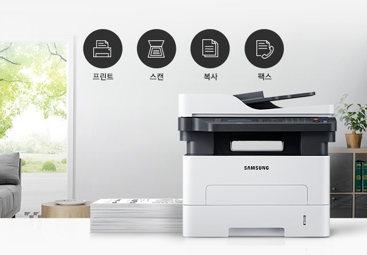 이미지 왼쪽에는 푸른 나무가 보이는 창문과 회색 소파가 배치되어 있으며, 이미지 오른쪽에는 제품 정면 이미지가 배치되어 있습니다. 제품 이미지 왼쪽에는 종이가 쌓여 있으며, 제품 이미지와 소파 사이에는 프린터 텍스트와 프린터 아이콘, 스캔 텍스트와 스캔 아이콘, 복사 텍스트와 복사 아이콘, 팩스 텍스트와 팩스 아이콘이 왼쪽에서 오른쪽으로 나열하여 있습니다.