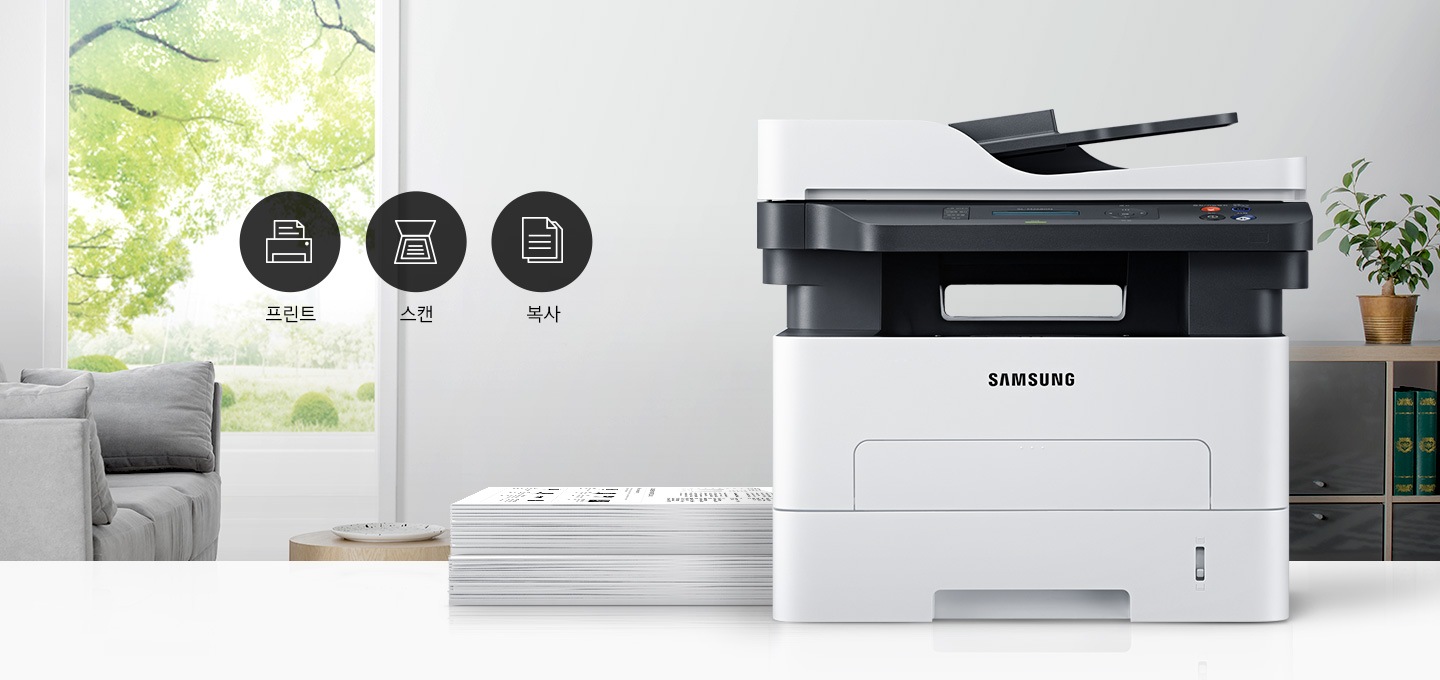 이미지 왼쪽에는 푸른 나무가 보이는 창문과 회색 소파가 배치되어 있으며, 이미지 오른쪽에는 제품 정면 이미지가 배치되어 있습니다. 제품 이미지 왼쪽에는 종이가 쌓여 있으며, 제품 이미지와 소파 사이에는 프린터 텍스트와 프린터 아이콘, 스캔 텍스트와 스캔 아이콘, 복사 텍스트와 복사 아이콘, 팩스 텍스트와 팩스 아이콘이 왼쪽에서 오른쪽으로 나열하여 있습니다.