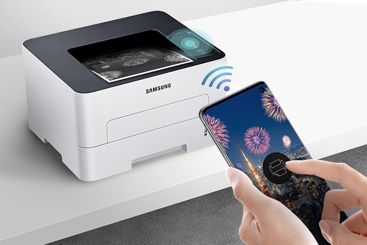 하얀색 책상 위에 제품을 왼쪽 위에서 내려본 이미지가 중간에 배치하여 있고 이미지 오른쪽 부분에 스마트폰 화면에 프린터 아이콘을 누르고 있는 사람의 손이 배치하여 있습니다.