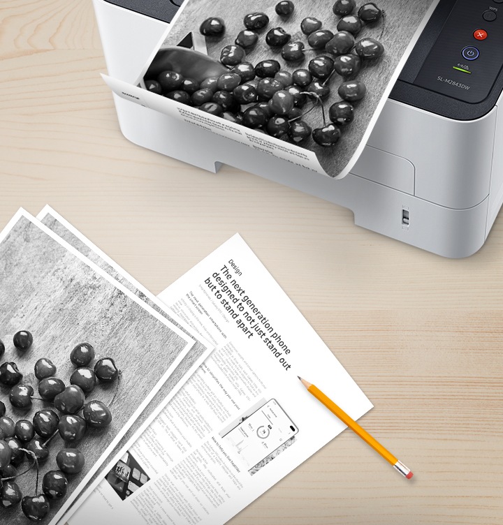 나무 책상 위 배경에 오른쪽 위에는 출력물이 출력되고 있는 제품을 위에서 내려본 이미지가 있고 출력물은 안쪽 부분에 텍스트가 있는것이 보여지고 있어 양면으로 인쇄를 할 수 있는 것을 알려주고있습니다. 이미지 왼쪽 하단에는 이미 출력된 출력물이 나열되어 있습니다.