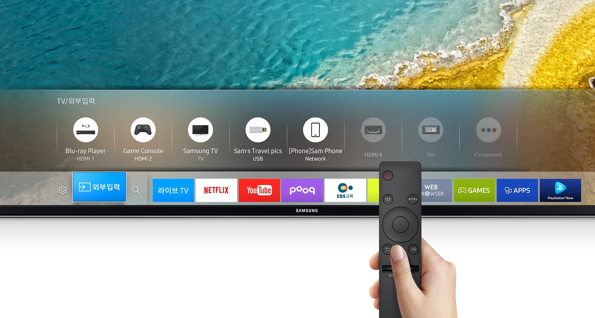 화면의 상단에 삼성 UHD TV가 확대되어 나타나 있습니다. 제품은 하단부분만 확대되어 나타나 있으며, 해변배경의 화면 위로 TV/외부입력, 콘텐츠들이 bar 형태의 메뉴로 나타나 있습니다. 그런 제품의 위로 오른손으로 검정 색상의 TV리모컨을 쥐고 있는 모습이 보여집니다.