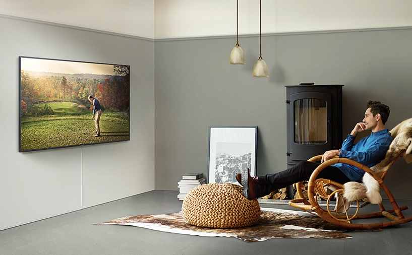 TV가 벽에 걸려있고 남성이 앉아서 시청하고 있습니다.