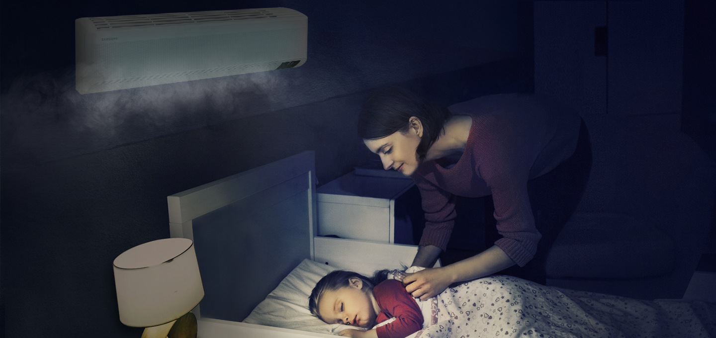 에어컨이 설치된 방에서 여성이 침대에 누워 자고 있는 아이를 바라보는 모습이 보입니다.