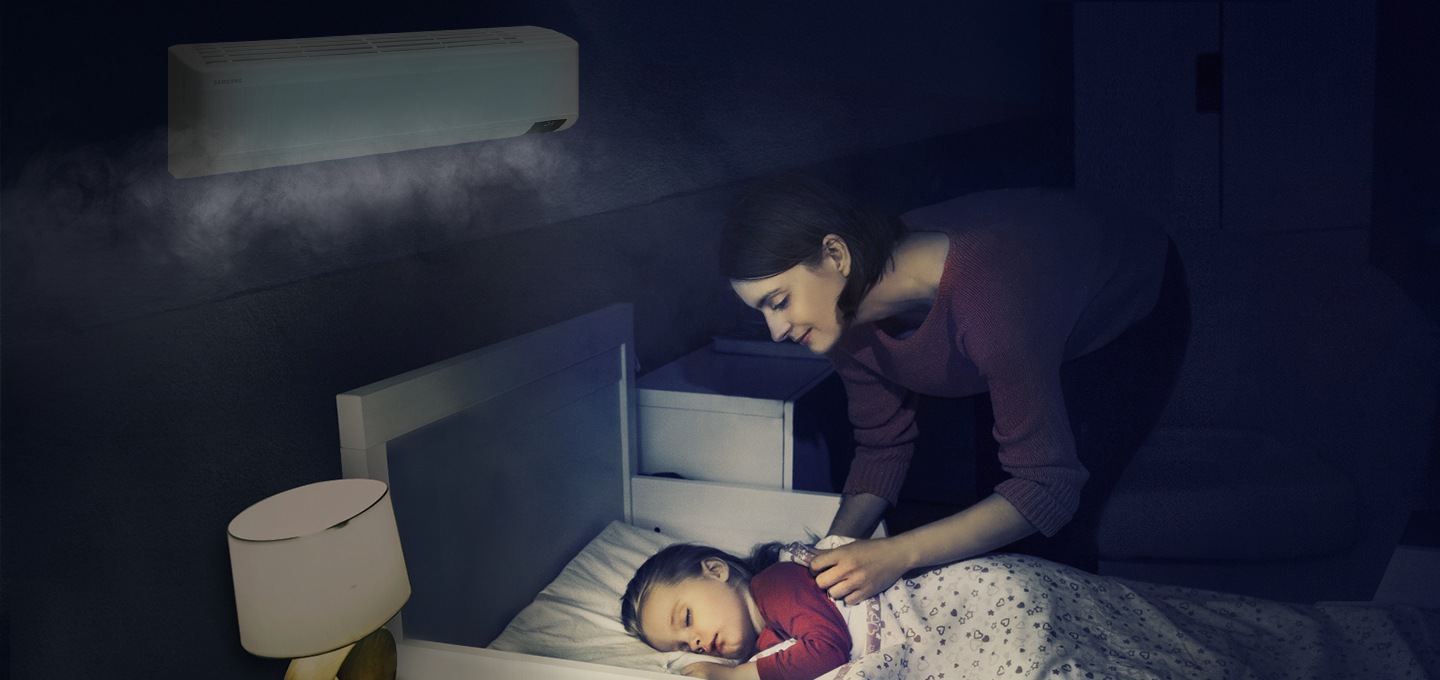 에어컨이 설치된 방에서 여성이 침대에 누워 자고 있는 아이를 바라보는 모습이 보입니다.