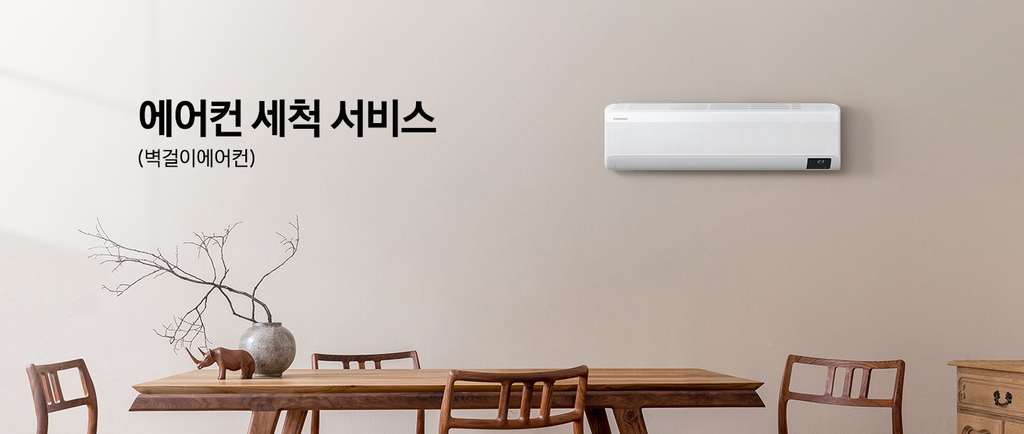 베이지톤 넓은 주방과 우드 식탁이 배치되어 있으며, 벽면 우측에는 삼성 벽걸이형 에어컨 실내기가 설치되어 있습니다. 이미지 좌측 상단에는 에어컨 세척 서비스 (벽걸이에어컨) 이라는 타이틀 텍스트가 있습니다.