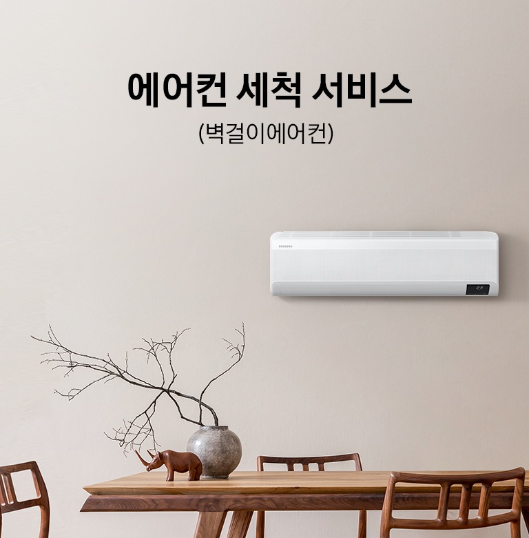 베이지톤 넓은 주방과 우드 식탁이 배치되어 있으며, 벽면 우측에는 삼성 벽걸이형 에어컨 실내기가 설치되어 있습니다. 이미지 좌측 상단에는 에어컨 세척 서비스 (벽걸이에어컨) 이라는 타이틀 텍스트가 있습니다.