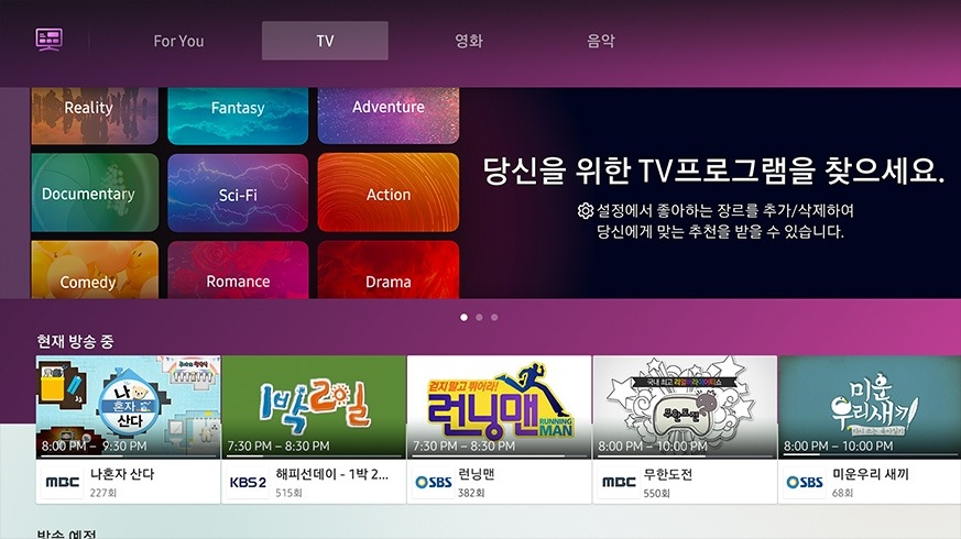 흰 배경에 QLED TV가 정면으로 놓여져 있습니다. 화면 안에는 TV 채널을 추천해주는 TV 콘텐츠가 보여집니다. TV 뒤 좌/우측엔 순서대로 For You 컨텐츠, 영화 컨텐츠가 보여집니다.