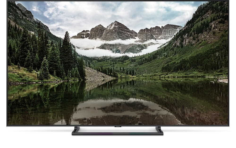 QLED TV 제품이 정면으로 놓여져 있고 화면 안에는 중앙의 호수를 산이 둘러싸고 있는 이미지가 흐리게 보여집니다.