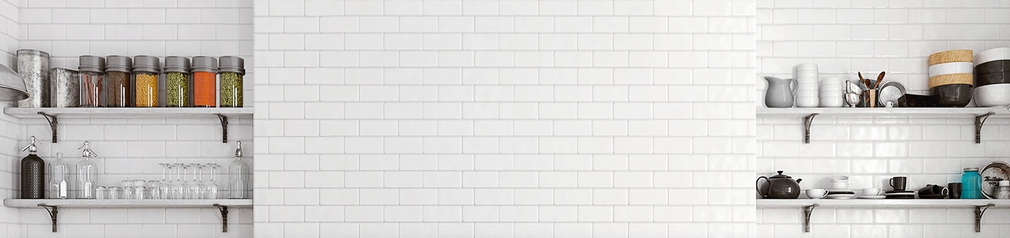 흰색 타일로 마감된 주방의 벽면이 보이고 이미지 양쪽 끝엔 다양한 그릇과 용기들이 놓여져 있는 선반이 있습니다.