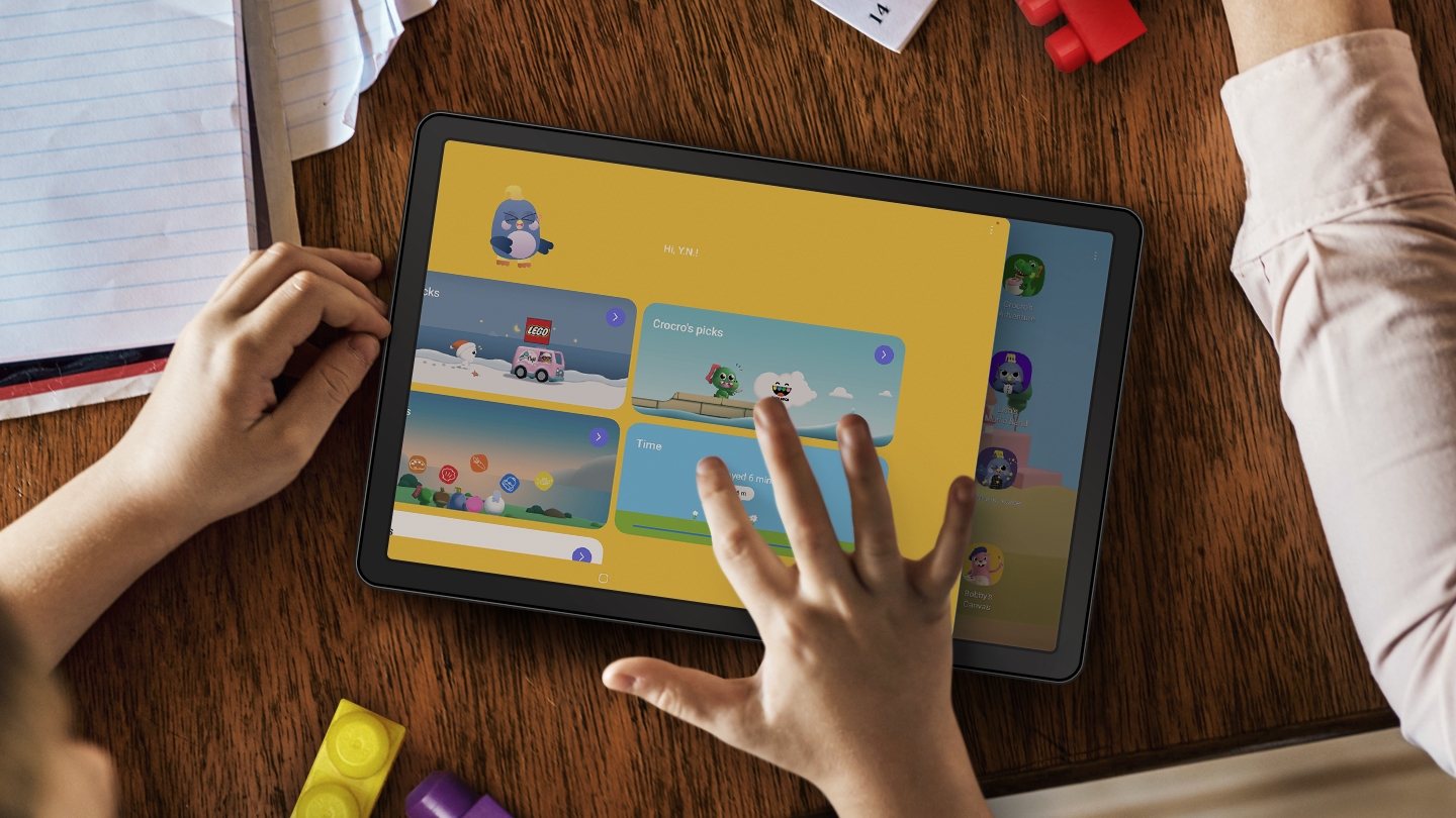 탁자 위에 종이와 LEGO 블록으로 둘러싸인 태블릿의 연출된 이미지. 가까이에 어린이의 손이 보이며 오른손이 태블릿 화면을 터치하고 있습니다. 화면에는 자녀가 경험할 수 있는 다양한 종류의 엔터테인먼트를 보여주는 LEGO 앱 UI가 표시되어 있습니다.