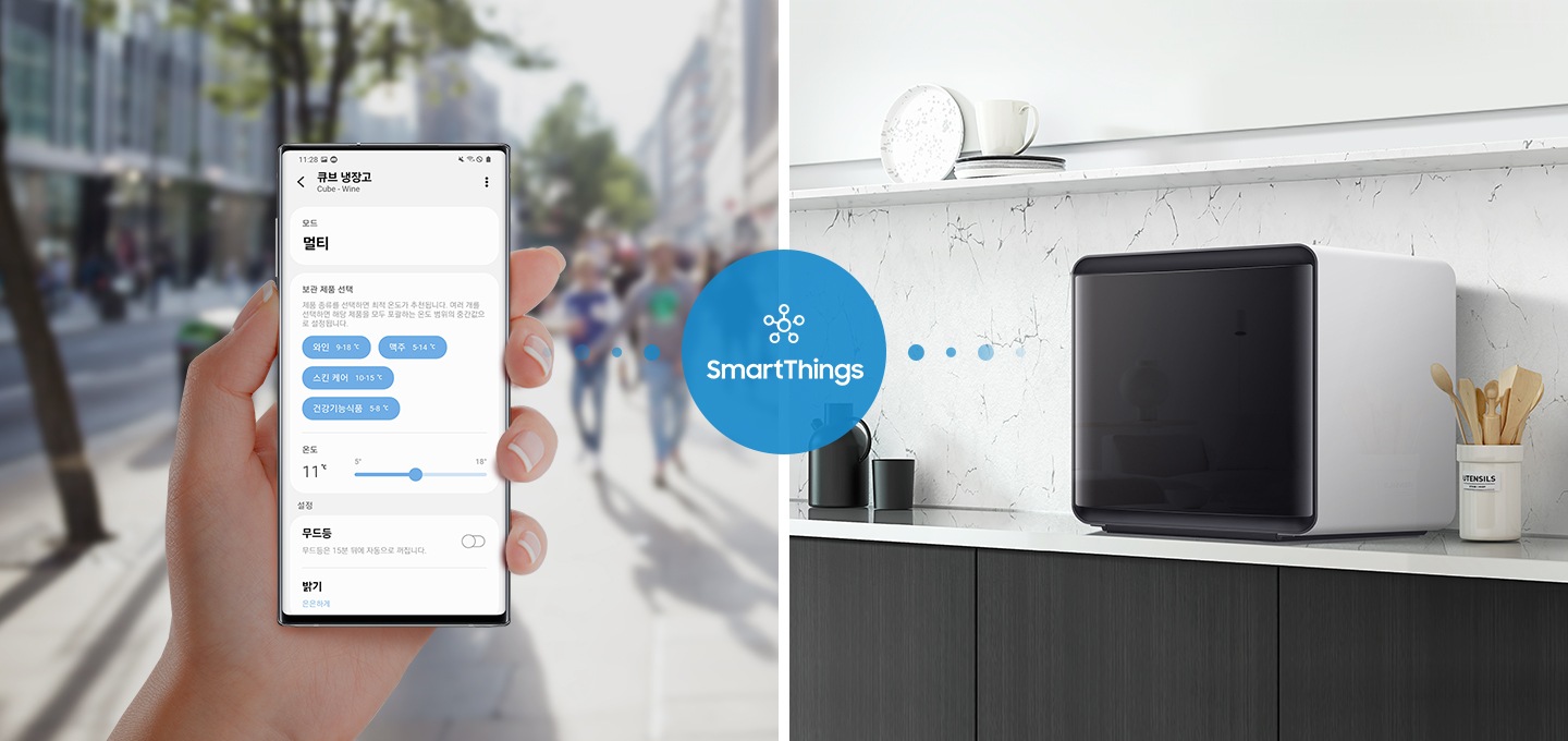 좌측에는 휴대폰을 쥐고 있는 손 사진이 나와있습니다. 휴대폰 화면애는 SmartThings 큐브 냉장고 화면이 나와있으며 모드와 온도, 보관 제품 선택 등의 옵션이 보여집니다. 가운데 SmartThings  로고와 문구가 파란 원 안에 있으며 우측 화이트톤 인테리어컷 선반 위에 설치된 BESPOKE 큐브 냉장고와 연결되고 있는 이미지입니다.