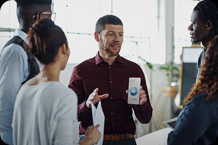 여러 명의 사람이 모여 이야기를 하고 있습니다. 한 남자가 도넛형 그래프가 보이는 갤럭시 S21 Ultra 5G를 들고 있습니다.
