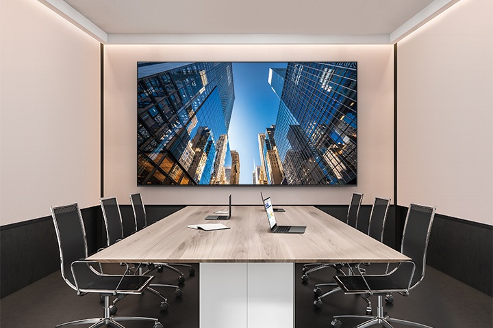 회의실 공간에 회의테이블과 의자가 있고 정면 벽 중앙에는 단독형 UHD E 시리즈가 설치되어 있습니다.