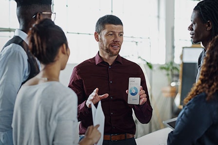 여러 명의 사람이 모여 이야기를 하고 있습니다. 한 남자가 도넛형 그래프가 보이는 갤럭시 S21 Ultra 5G를 들고 있습니다.