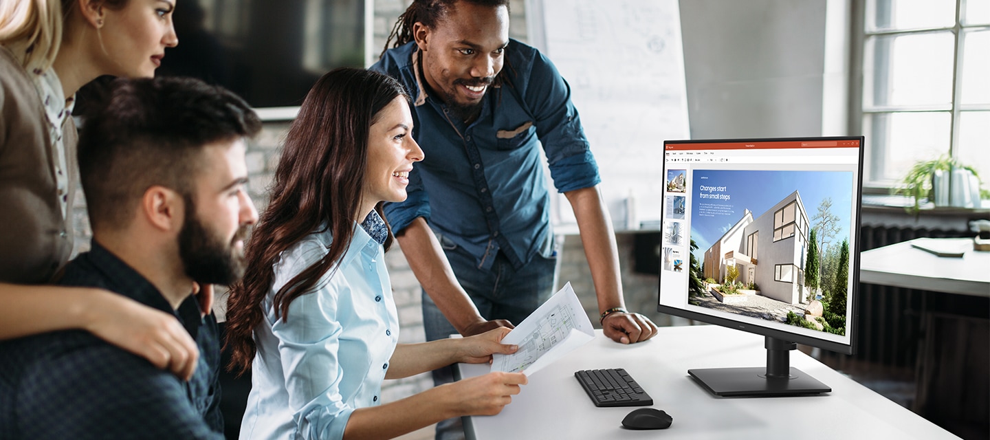 책상 위에 키보드 및 마우스와 모니터가 보입니다. 모니터 화면에는 건물이 잘 보이는 풍경이 보입니다. 모니터 앞에는 여성이 설계도를 양 손에 쥔 채 모니터를 웃으며 바라보고 있습니다. 이 여성 주위로 남성 2명과 여성 1명이 함께 모니터를 바라보고 있습니다.