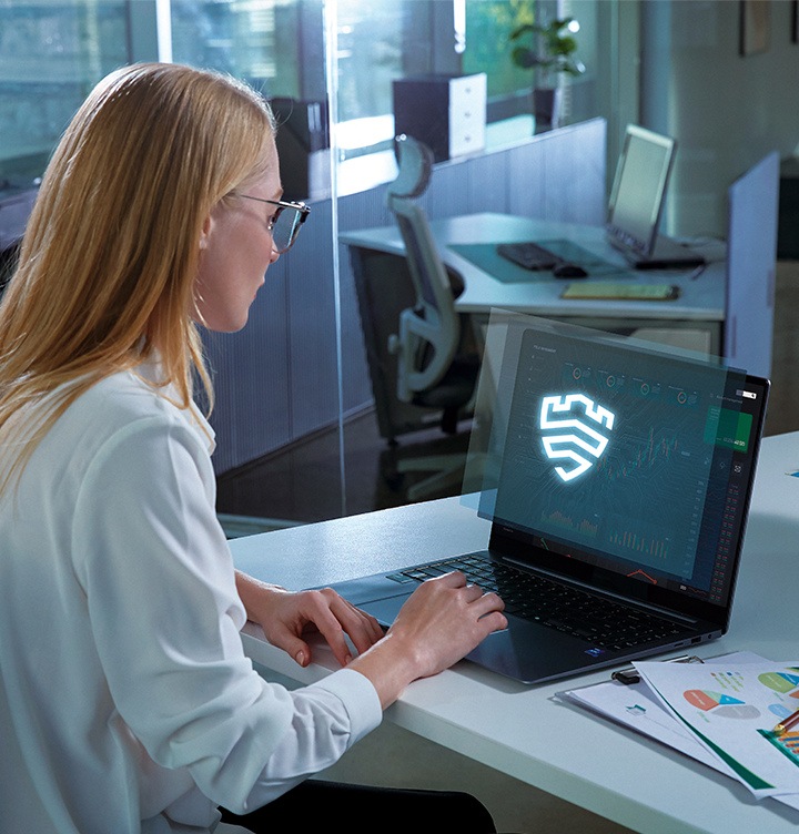 [깔끔하고 모던한 사무실에서 안경을 쓴 여성이 책상에 놓여진 갤럭시 북 앞에 앉아 있습니다. 화면에는 큼직한 삼성 Kñóx~ Váúl~t 로고가 표시되어 있습니다.]