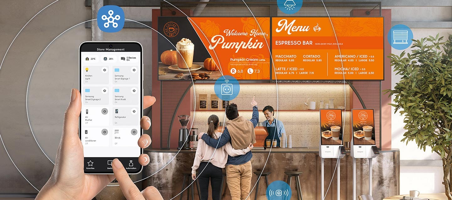 카페 카운터에서 비즈니스TV에 보이는 메뉴를 보고있는 남녀의 뒷모습이 있고, 좌측에는 스마트폰의 스마트싱스로 화면을 조절하고 있는 손이 보입니다.