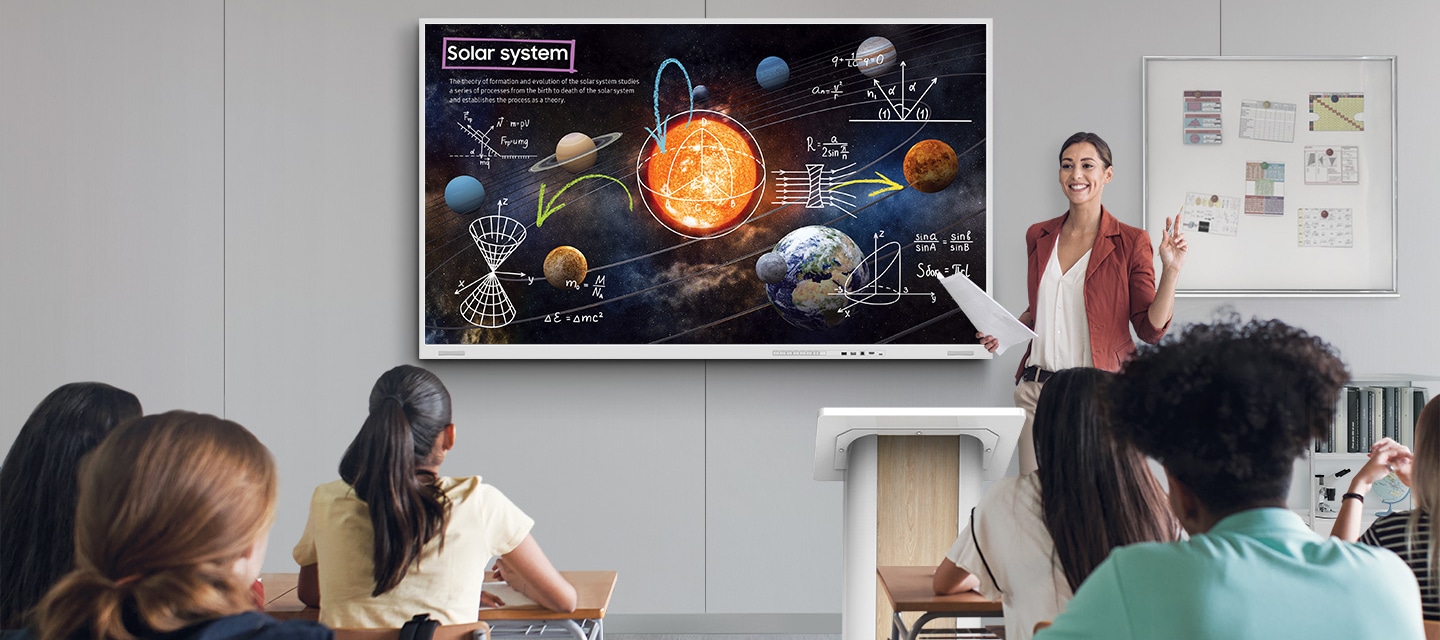 교실 벽면에 사이니지가 설치되어 있고, 교사가 사이니지 전자칠판 화면에 메모를 하며 수업을 진행하는 모습.