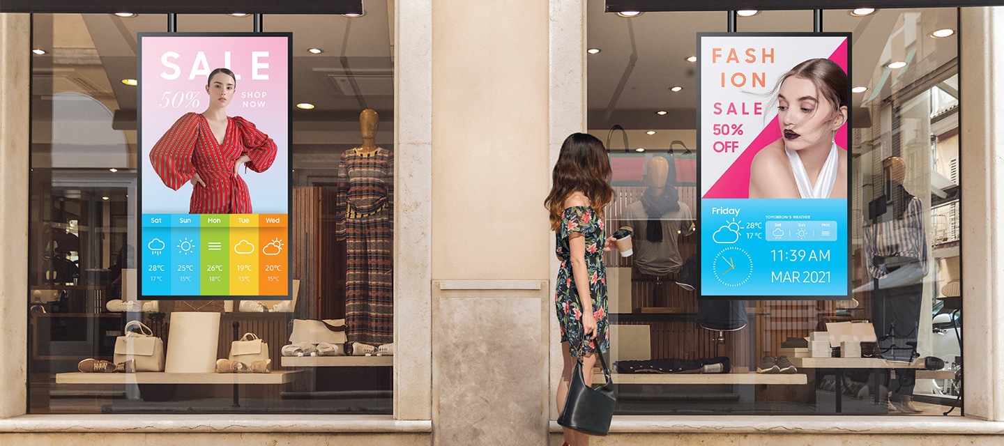 [의류매장 창에 배치된 사이니지를 통해 광고 컨텐츠가 송출되고 있으며, 이를 보고있는 한 여성의 모습이 보입니다.]