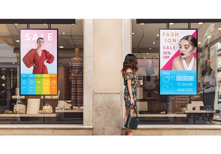 [의류매장 창에 배치된 사이니지를 통해 광고 컨텐츠가 송출되고 있으며, 이를 보고있는 한 여성의 모습이 보입니다.]