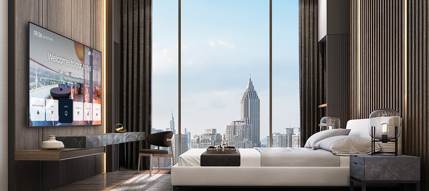 바깥 도시풍경이 보이는 고급스러운 호텔방의 침대 정면에 삼성 호텔TV가 설치되어 있고, 화면으로 호텔의 안내 화면이 송출되고 있는 모습입니다.