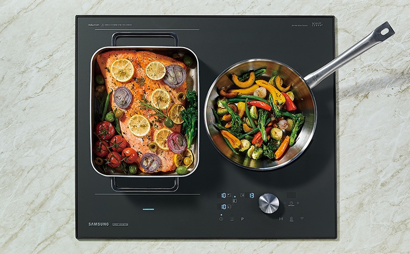 대리석으로 된 조리대 위에 전기레인지가 빌트인 방식으로 설치되어 있으며 이를 위에서 정면으로 내려다본 모습입니다. 전기레인지의 왼쪽 플렉스존에는 연어 스테이크, 오른쪽 플렉스존에는 조개찜을 조리중입니다.