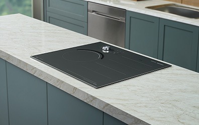 대리석으로 된 조리대 위에 전기레인지가 빌트인 방식으로 설치된 모습입니다. 뒤로 주방 용품과 싱크대가 보입니다.