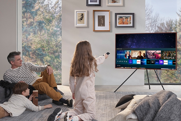 사용자들이 거실에 앉아서 TV 를 보고 있습니다. TV 에는 다양한 OTT 서비스들이 보이고 있습니다.