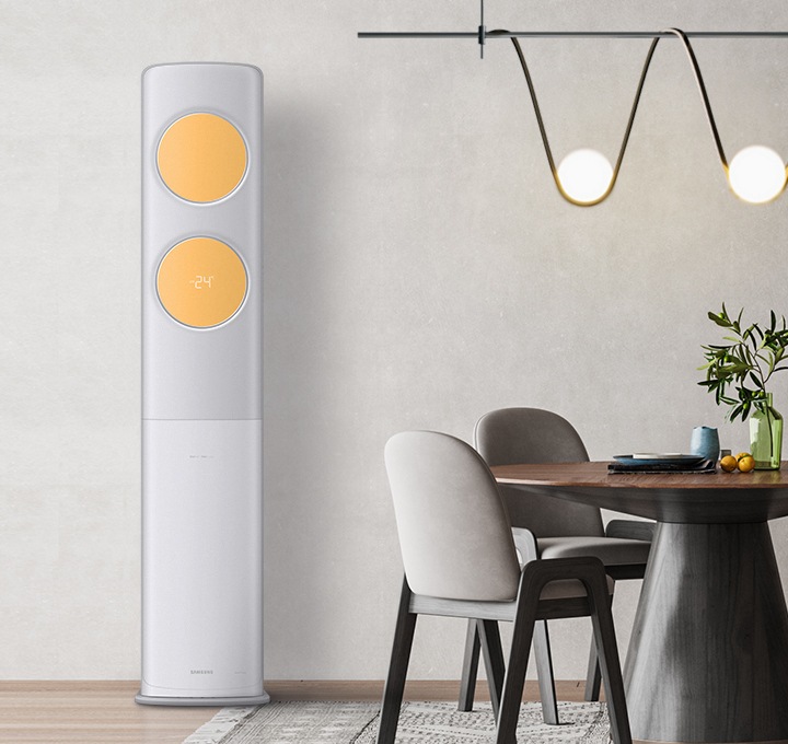 베이지톤의 벽면과 그레이톤의 패브릭이 깔려있는 거실에 짙은 브라운과 그레이 컬러의 3인용 테이블과 의자가 놓여져 있습니다. 테이블의 왼편에 비스포크 무풍에어컨 클래식이 설치되어있습니다. 바람문의 컬러는 밝은 옐로우 컬러이며, 테이블 위에는 모던한 전구, 뒷편에는 아치형의 큰 거울이 테이블의 한쪽 면을 비추고 있습니다. 