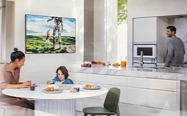 주방에 벽걸이 TV 가 설치되어 있습니다. 여성과 아이가 식탁에 앉아있습니다.