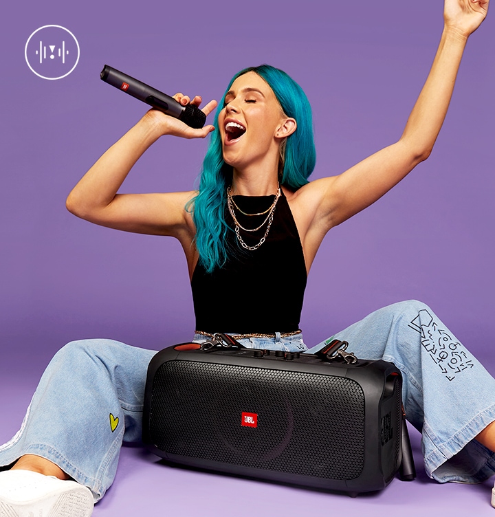 여성 사용자가 바닥에 앉아있고 무선 마이크를 들고 있습니다. 사용자 앞에는 PARTYBOX 스피커 제품이 놓여있습니다.