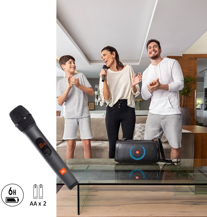 가족 사용자들이 거실에 서 있습니다. 탁자에는 PARTYBOX 스피커가 놓여있고 좌측에는 무선 마이크 와 배터리 아이콘, AA 건전지 아이콘이 보입니다.