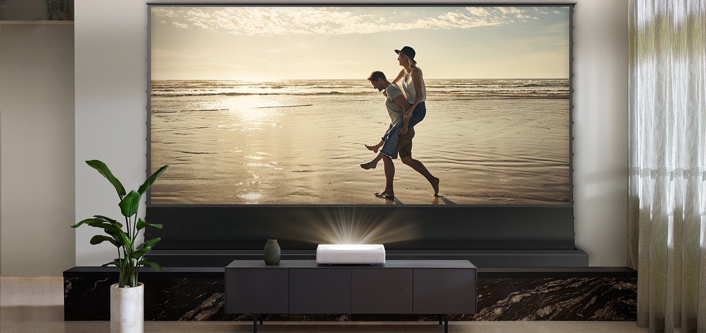선반위에 The Premiere 와 롤러블 스크린 블랙 제품이 설치되어 있고 화면에는 해변 화면과 남성과 여성이 보입니다.