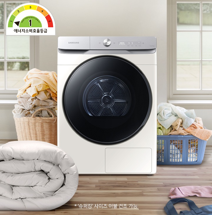 원목 우드로 된 바닥위에 삼성 건조기 제품과 이불, 빨래, 여자아이가 빨래 바구니를 뒤집어 쓰고 있습니다.