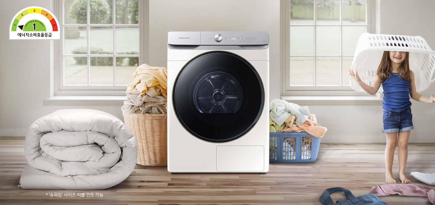 원목 우드로 된 바닥위에 삼성 건조기 제품과 이불, 빨래, 여자아이가 빨래 바구니를 뒤집어 쓰고 있습니다.