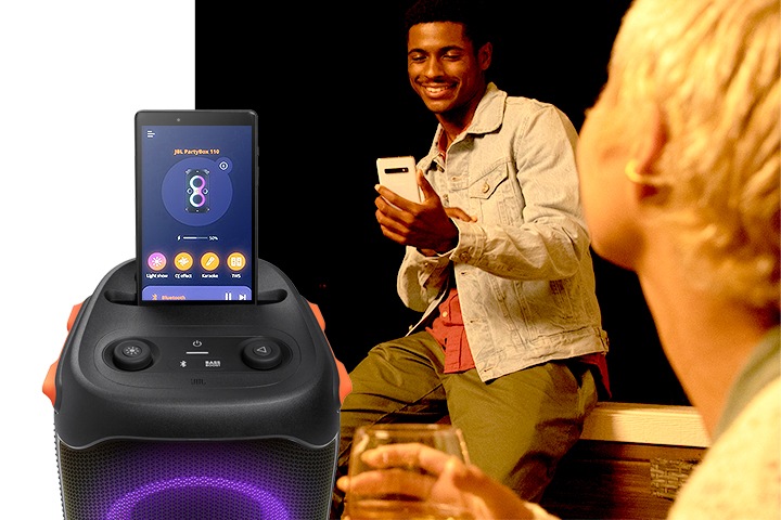 남성 사용자가 스마트폰을 보고 있습니다. 좌측에는 PARTYBOX 110 제품의 정면컷이 보이고 있고 상단에 태블릿이 연결되어 있습니다. 화면에는 PARTYBOX 110 제품의 온스크린이 보입니다.