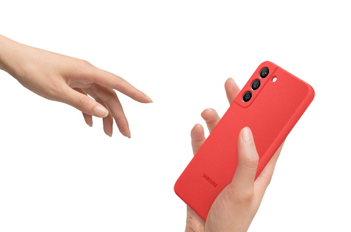 갤럭시 S22+ 실리콘 커버 코랄 색상을 한 손으론 쥐고 있고, 반대손으론 실리콘 커버를 잡기 위해 다가가고 있습니다.