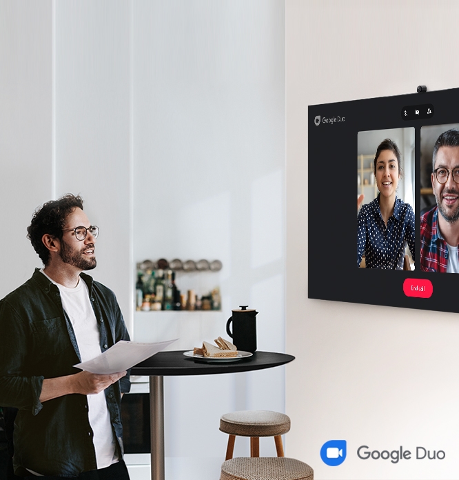 좌측 이미지는 벽걸이 TV가 설치되어 있고, 남성이 서서 TV를 바라보고 있습니다. TV 화면속에는  화상회의를 하는 모습이 보입니다. 우측 하단에는 구글 듀오 아이콘이 있습니다.