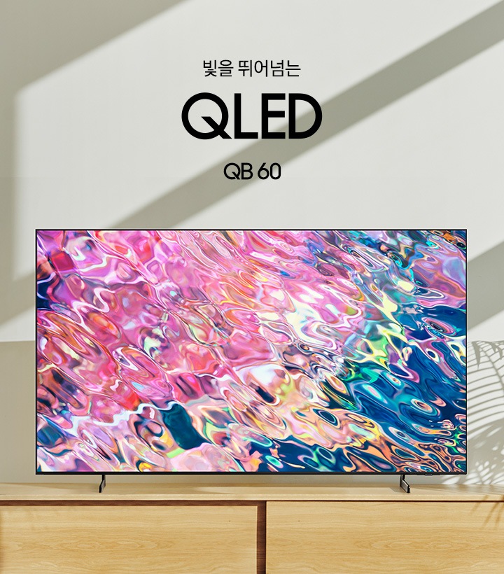 서랍장 위에 TV가 놓여있고 화면에는 핑크색 물결 화면이 보입니다. 빛을 뛰어넘는 QLED QB60 KV 입니다. 하단 3 pod 에는 번인 걱정없는 퀀텀 디스플레이 4K 문구와 반짝이는 디스플레이 아이콘, 인공지능으로 완성한 AI 퀀텀 사운드 문구와 TV아이콘에서 사운드가 나오는 그래픽 효과 아이콘, 삼성 TV 로 완성되는QLED 홈라이프 문구와 TV와 리모컨, TV 속 컨텐츠들을 표현한 아이콘이 있습니다.