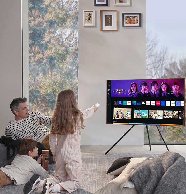 가족들이 앉아 TV 를 보고 있습니다. TV화면에는 다양한 OTT 서비스 화면들이 보입니다.