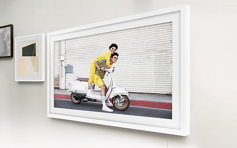 벽면에 The Frame 화이트 베젤로 설치된 이미지가 보입니다. 화면에는 남성, 여성이 스쿠터를 타고 있는 모습이 보입니다.
