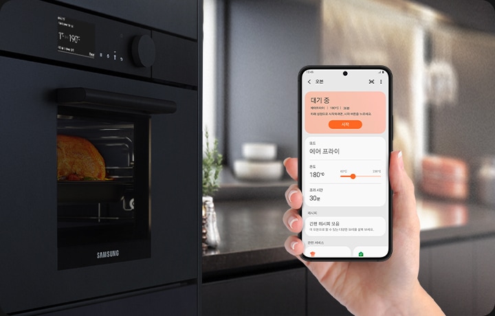 왼쪽에 빌트인 되어있는 오븐이있고, 오른쪽에는 핸드폰을 들고 있는 손이 있습니다. 핸드폰 디스플레이 안에는 스마트싱스 앱이 사용 되고 있고 맨 위에는 대기 중 문구와 함께 에어프라이 | 180도 | 30분 아래 설정으로 시작하려면, 시작 버튼을 눌러주세요. 시작 버튼이 활성화 되어있습니다. 그 아래에는 모드 > 에어 프라이, 온도 > 180도, 조리 시간 30분, 그 아래에 레시피 간편 레시피 모음 이 오븐으로 할 수 있는 다양한 요리를 살펴보세요. 문구가 있습니다.