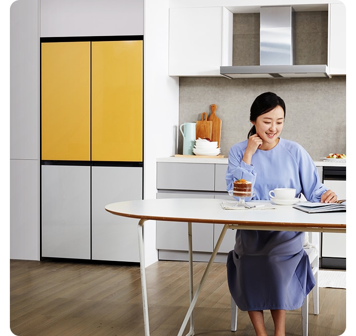 거실에 냉장고가 놓여져 있고, 여성이 의자에 앉아 책을 보고 있는 모습의 이미지입니다. 