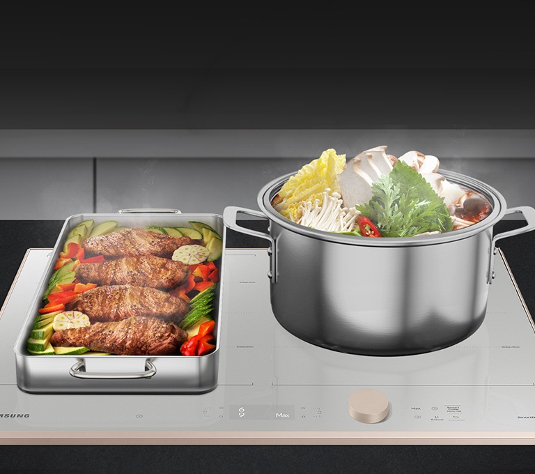 블랙 색상의 주방 상판에 설치된 BESPOKE 인덕션 빌트인 Infinite Line 그레이지 위로, 우측 화구에는 버섯이 들어간 찌개가 요리되고 있는 대형 양수 냄비가, 좌측 화구에는 채소와 생선이 요리중인 대형 사각 팬이 올려져 있습니다.